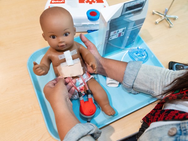 Akila holds a doll that has a plastic Ventricular Assist Device (VAD) attached. 