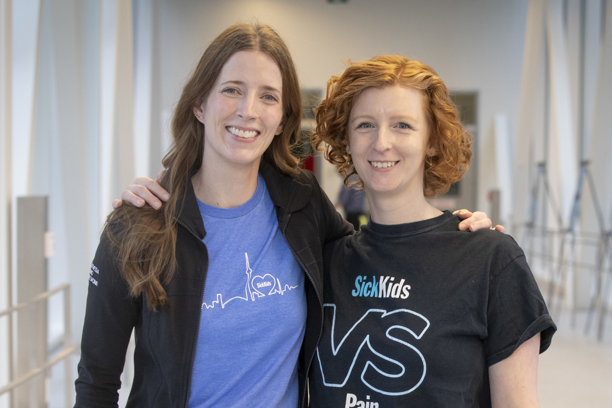 picture of ashley harvey and jacqueline hanleyst standing side by side with arms around each other in a bright indoor walkway with railings.