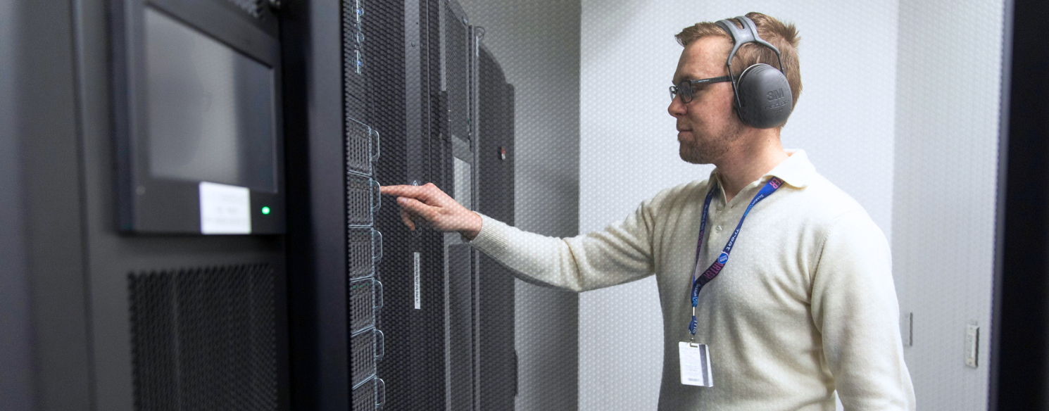 IT technician stands pointing at server rack in data centre